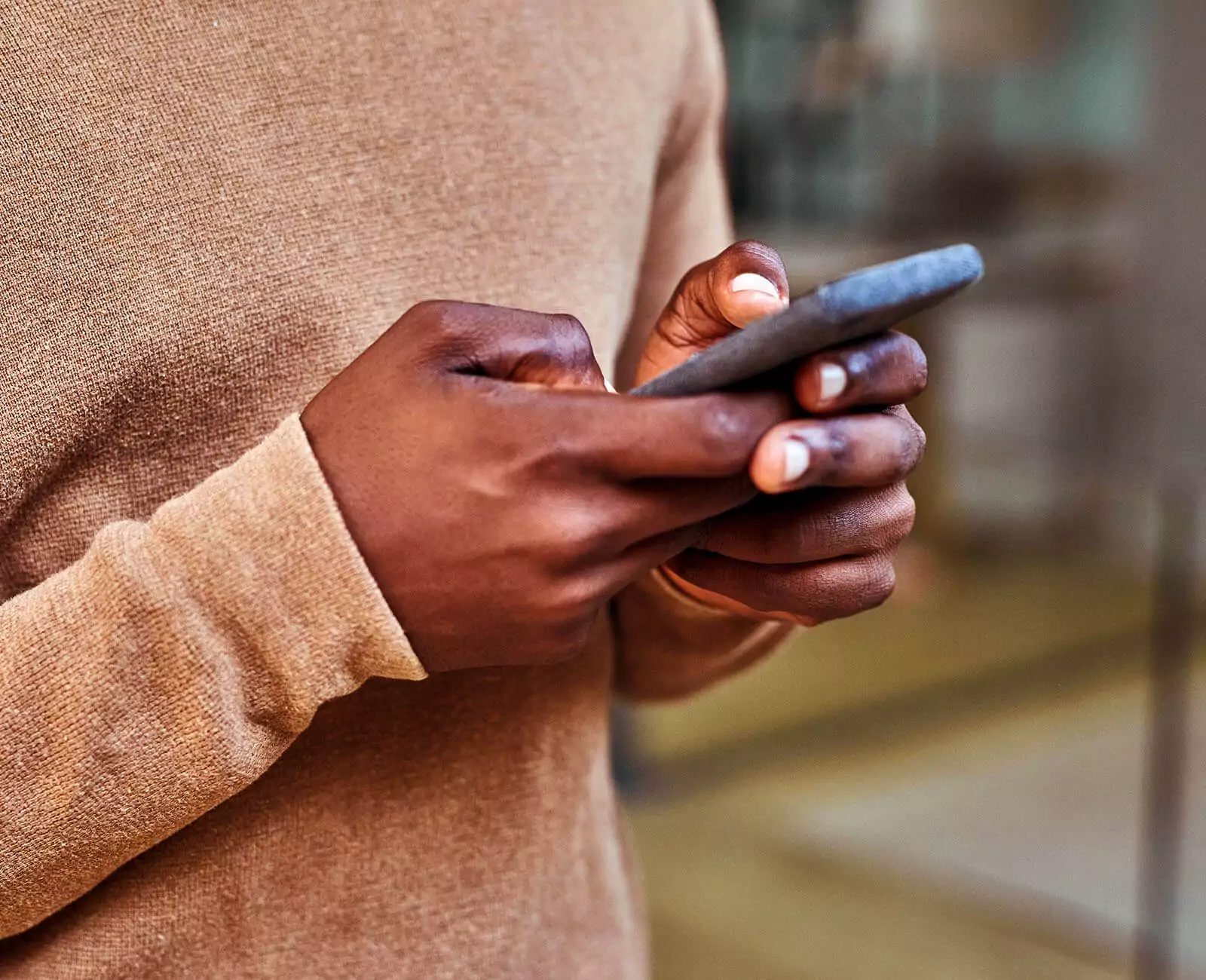 Close up of a person in light brown sweater holding a smartphone
