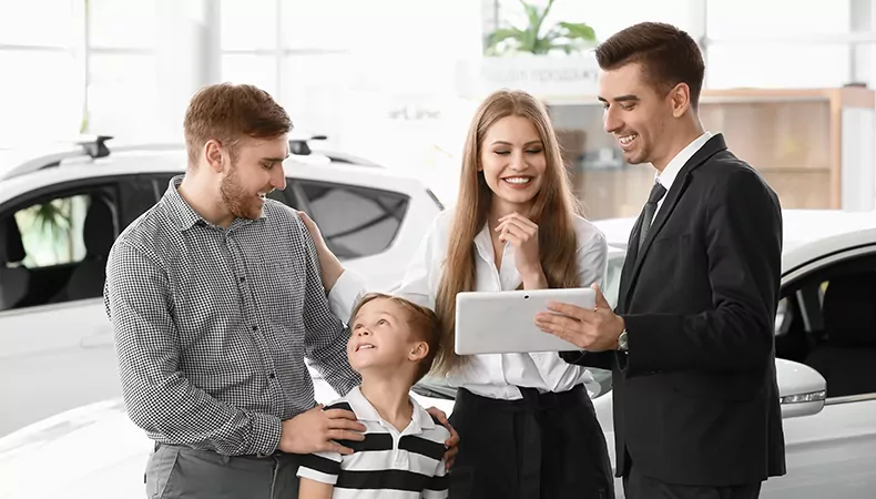 Salesman with tablet and young family in car salon